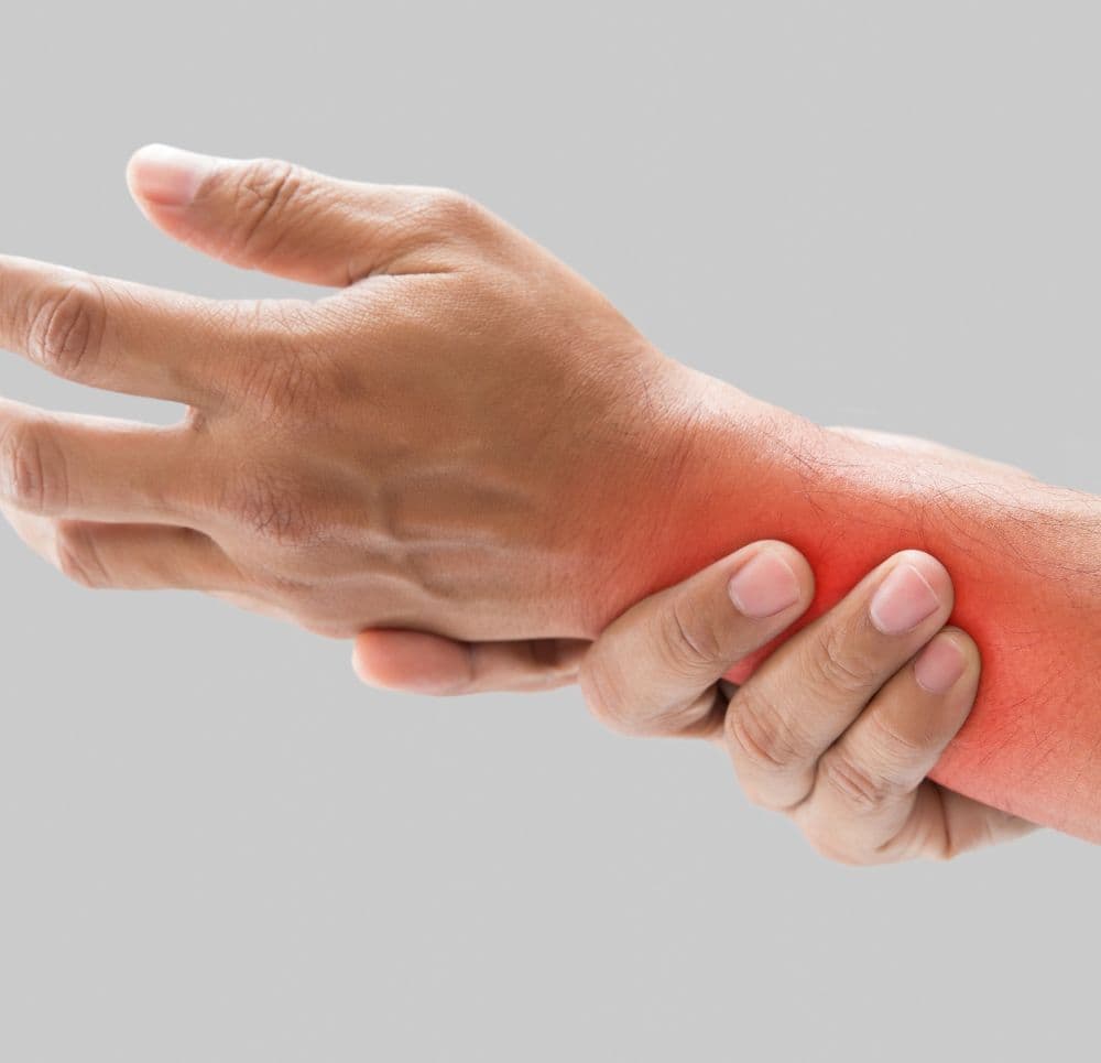 Zbliżenie na dłoń chwytającą bolesny nadgarstek z czerwonym polem sygnalizującym ból. Grafika obrazuje przyczyny drętwienia rąk oraz parestezje w obrębie dłoni i stawu.