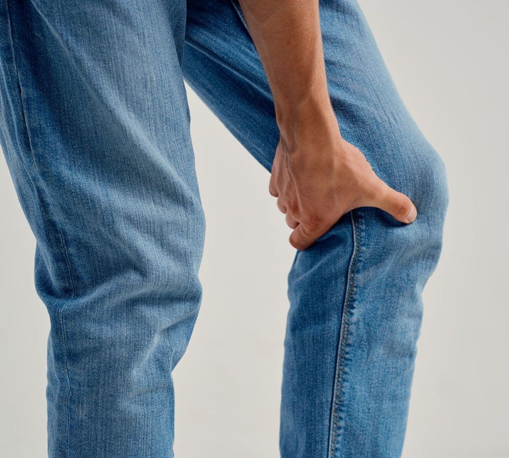 Osoba chwyta się oburącz za staw kolanowy w geście wskazującym na nagły ból lub kontuzję.