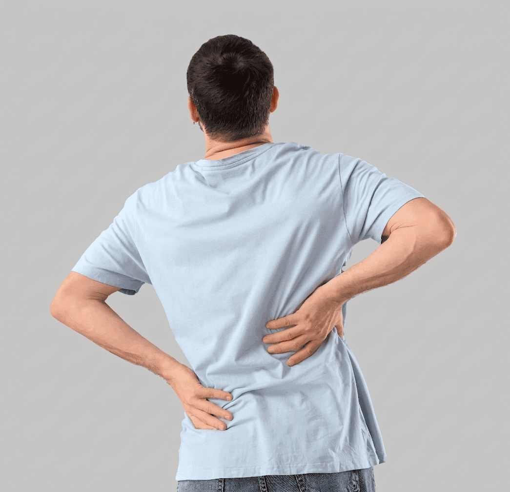 Mężczyzna widziany od tyłu w jasnoniebieskiej koszulce, trzymający się obiema rękami za dolną część pleców na wysokości lędźwi.