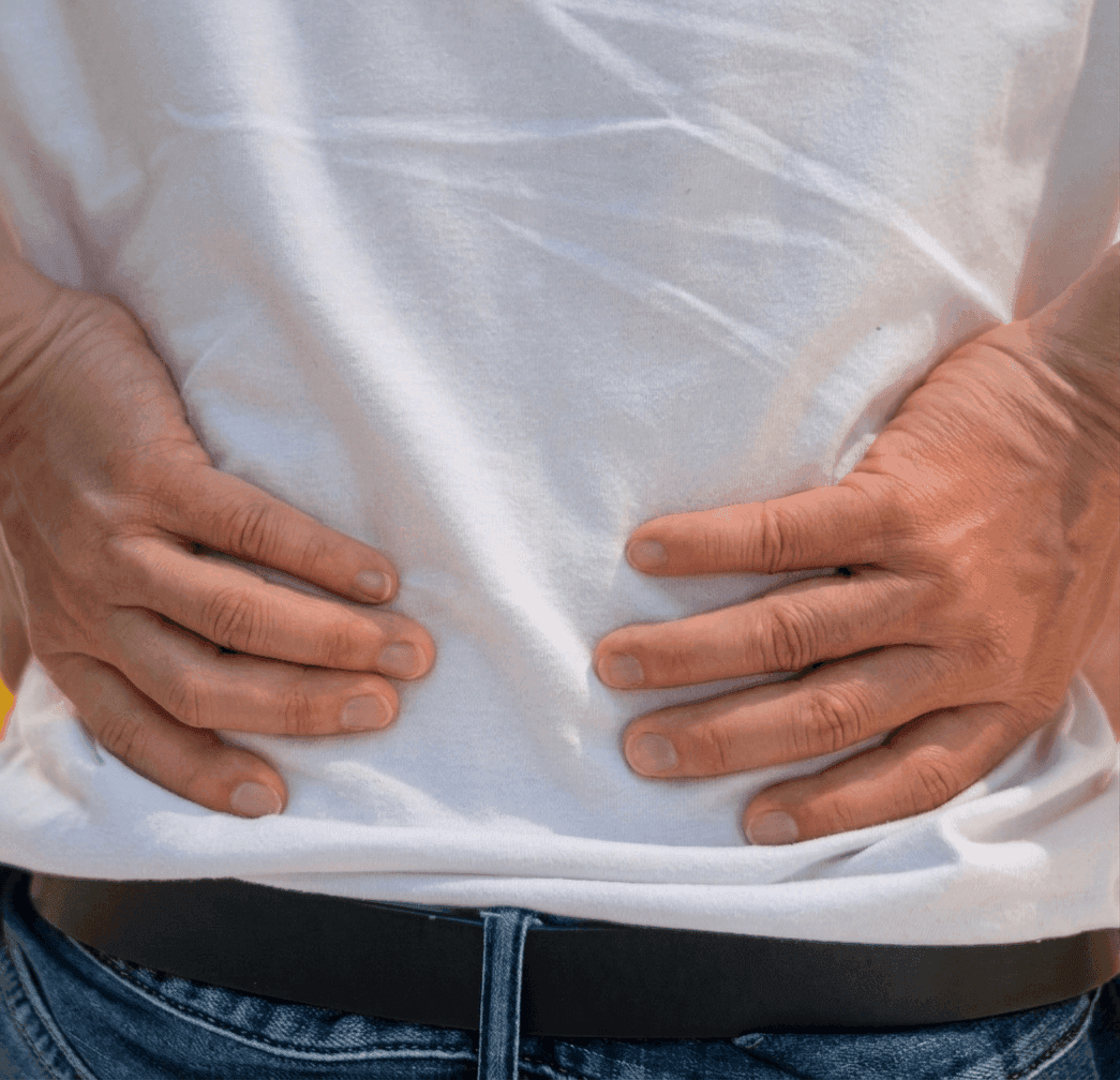 Zbliżenie na osobę trzymającą się obiema dłonią za bolesny dolny odcinek pleców, co sugeruje dyskopatię, ból kręgosłupa lub rwa kulszowa.