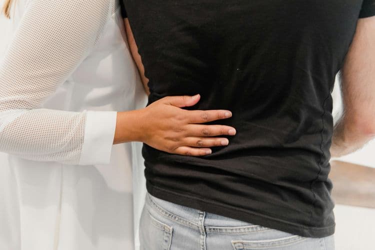 Kobieta trzyma dłoń na plecach mężczyzny cierpiącego z bólu wywołanym przez rwę kulszową.