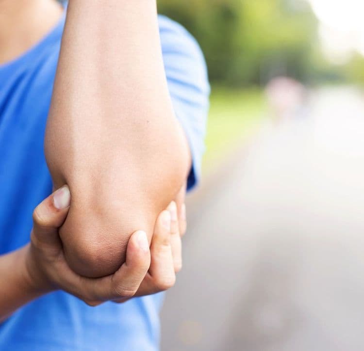 Mężczyzna z bólu trzyma się za staw łokciowy.