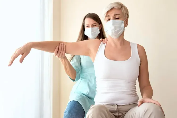 pacjentka z pomocą fizjoterapeuty unosi ramię w trakcie sesji ćwiczeń wspomaganych